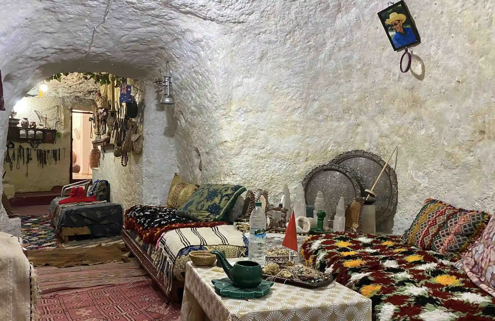 Lungo ambiente in grotta imbiancato a calce, arredato con panche, tappeti e un tavolino da tè