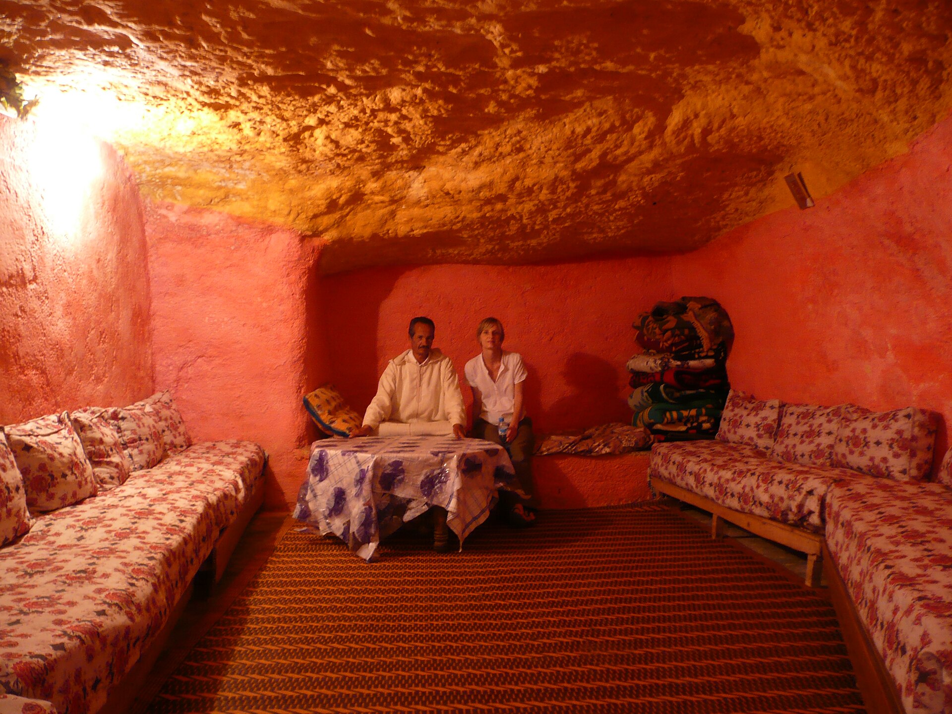 Proprietario e visitatore seduti insieme in un ambiente-grotta dai toni caldi a Bhalil